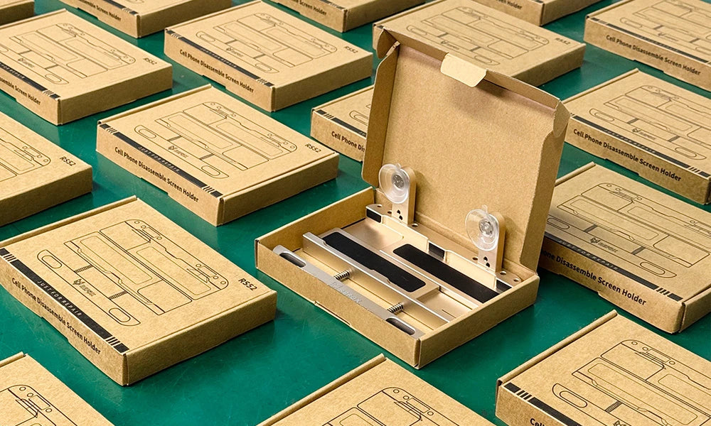 Open box with refox phone repair tools on a green surface surrounded by boxes.