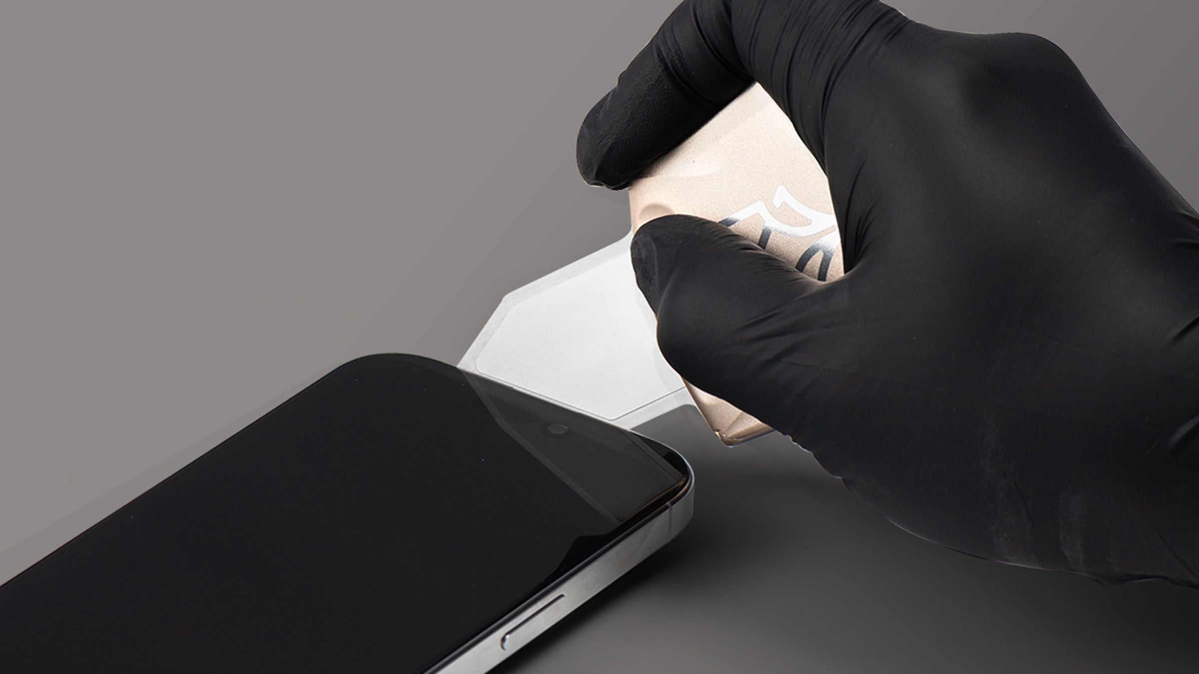 Hand wearing a black glove holding a smartphone on a gray background