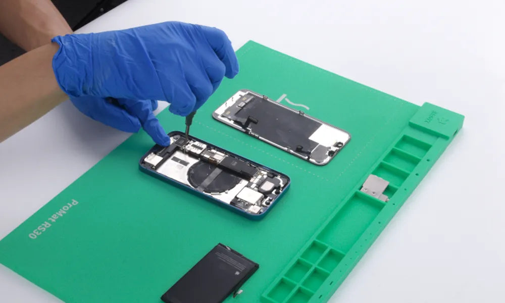 Person repairing a smartphone on a green work mat with tools.