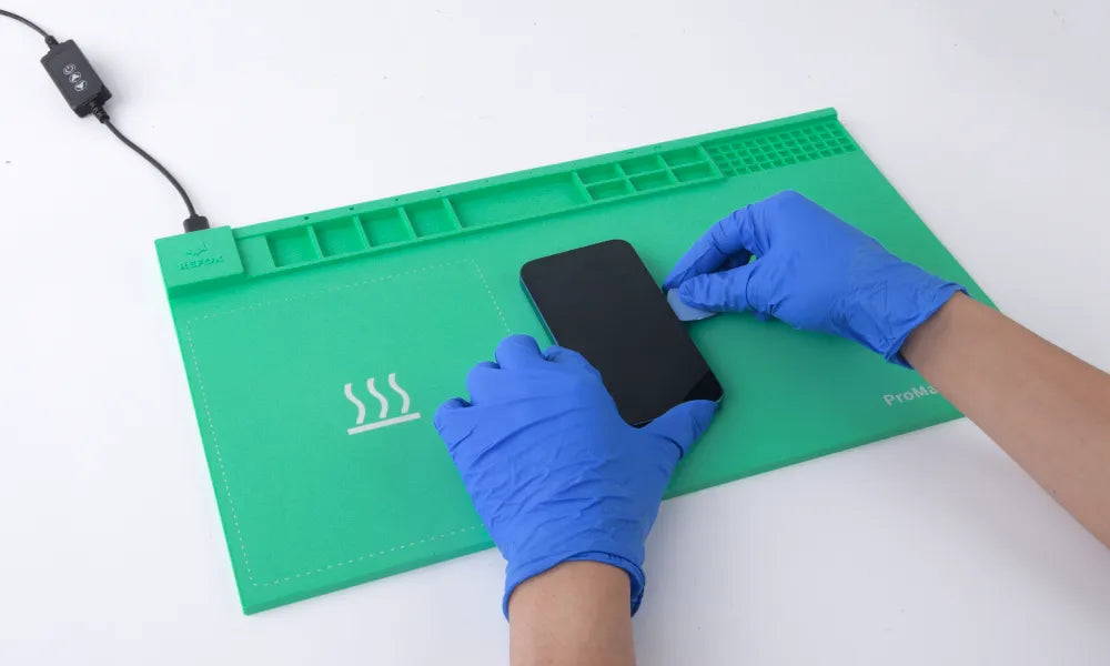 Person wearing blue gloves using a green rs30 mat with heating elements to handle a smartphone.