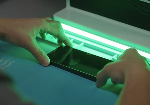 Person using a UV light box on a piece of paper with a green glow.