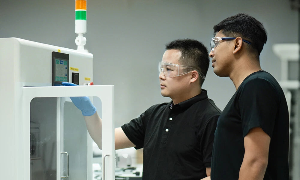 Two individuals in front of a refox machine, wearing safety goggles and gloves