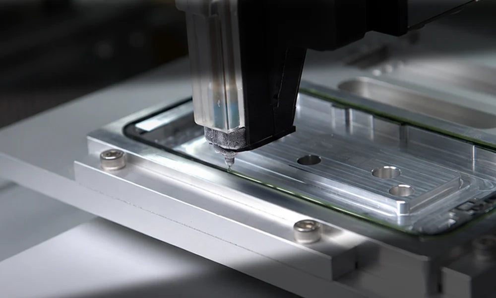 Close-up of a precision industrial machine arm depositing material onto a metallic silver substrate with a transparent protective film.
