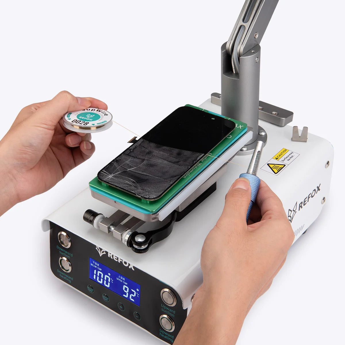 A REFOX mobile phone repair heat press machine with a screen placed on the green heating plate, being operated by two hands holding the control handles and temperature display.