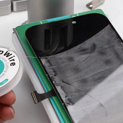 A close-up of a hand holding a spool of clear conductive wire next to a smartphone repair setup with a black screen protector and a green-and-white mounting board.