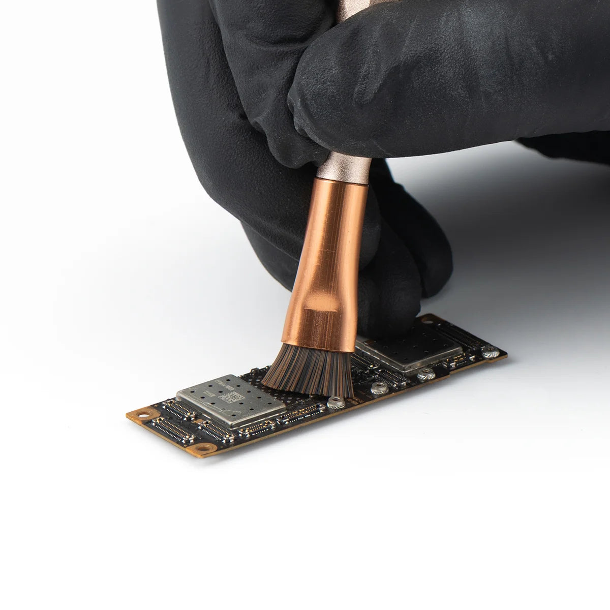 Person cleaning a phone motherboard with a brush on a white background