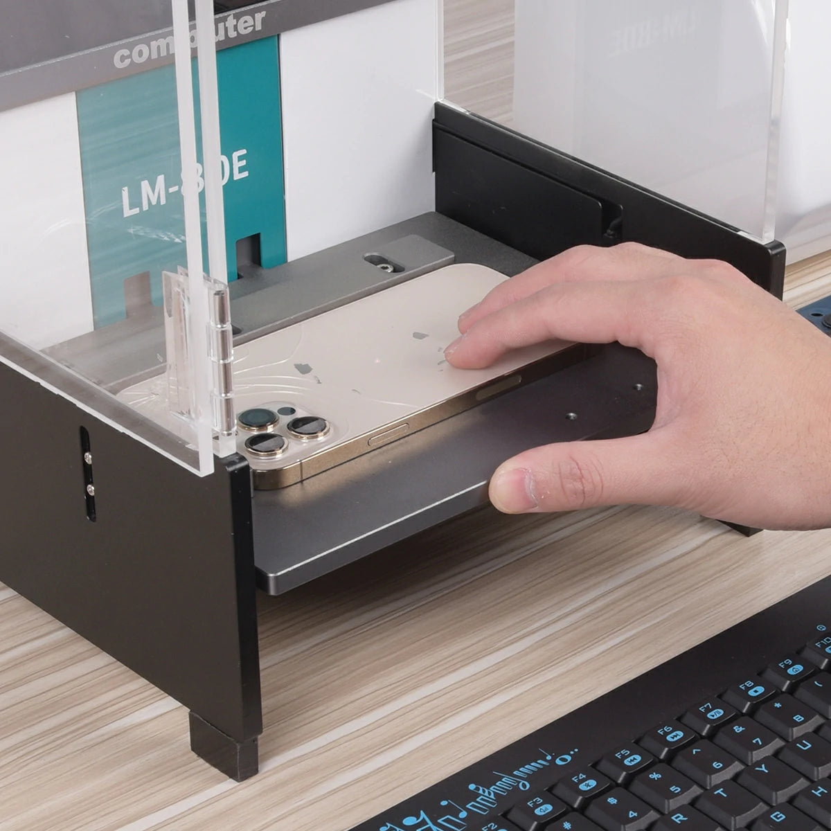 Hand placing a smartphone into a clear protective case on a desk with a keyboard in the foreground.