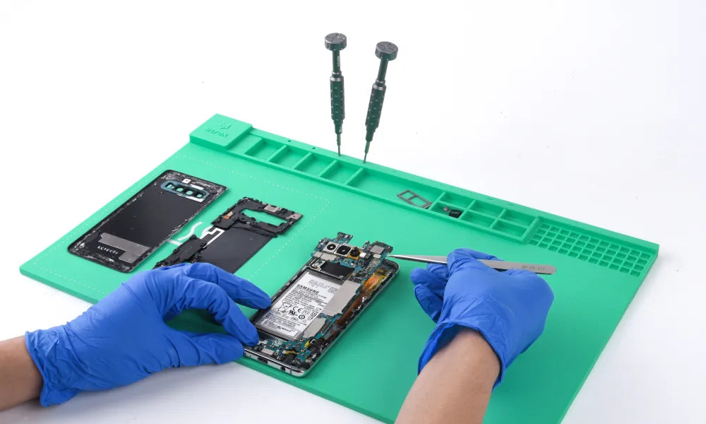 Person repairing a smartphone on a green work mat with tools